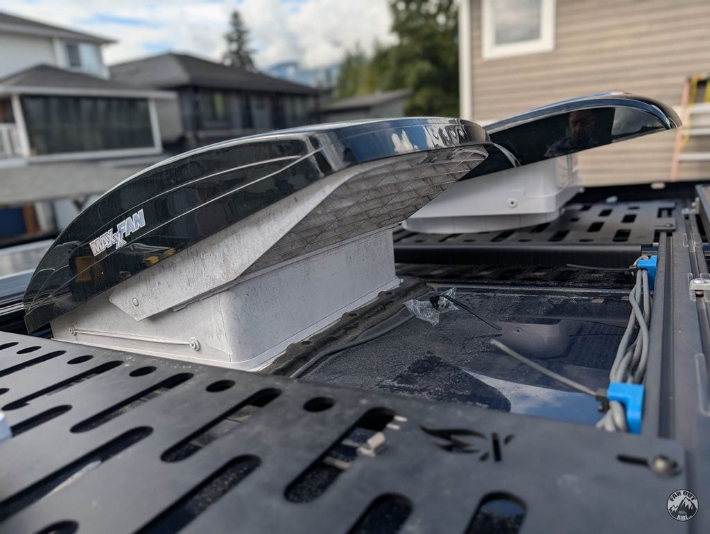 Maxxfan Deluxe in front and AirPlus behind, side by side on the van roof rack with both hooded lids open