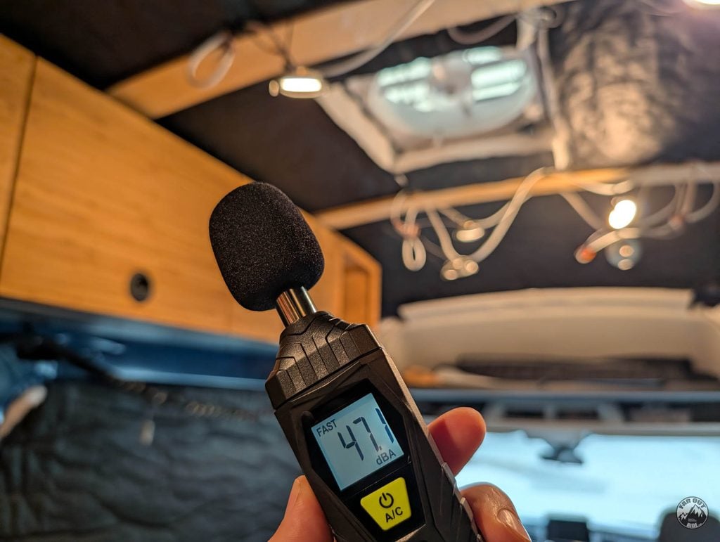 Handheld sound level meter reading 47.1 dBA inside the van, with the open roof fan in the ceiling behind it